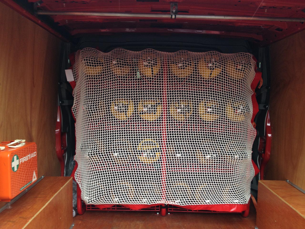 Heavy duty white cargo net with red PVC border used to restrain cylinders in an emergency service vehicle